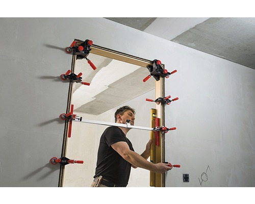 Muž montuje dvere do hrubej stavby pomocou šablóny zárubne dverí.