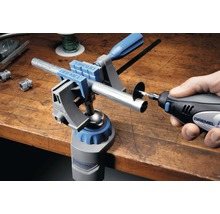 Logo spoločnosti Dremel. Pracovný stôl s multifunkčnými zverákmi Dremel a multifunkčným nástrojom Dremel na rezanie rúrky.