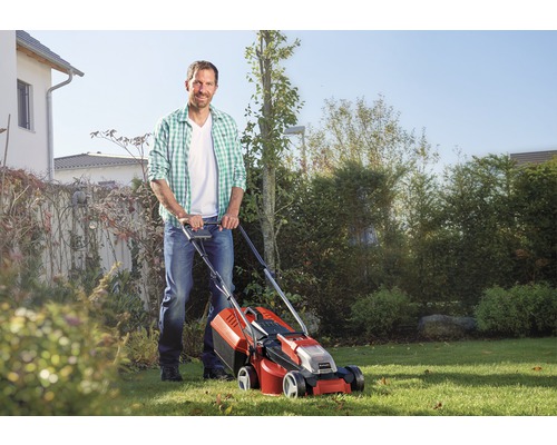 Muž používa kosačku na trávu v záhrade.