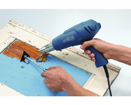 Osoba odstraňuje zvyšky farby z dverí pomocou teplovzdušnej pištole a špachtle