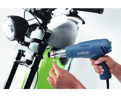 Osoba používa teplovzdušnú pištoľ Steinel HL 1620 S na motocykli.