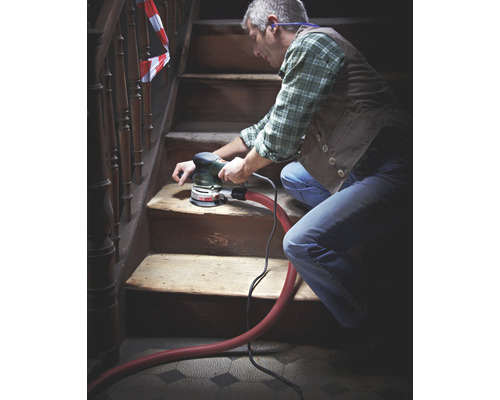 Muž brúsi drevené schodisko brúskou