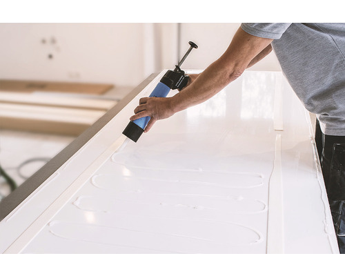 Remeselník nanáša lepidlo kartuší na biely povrch.