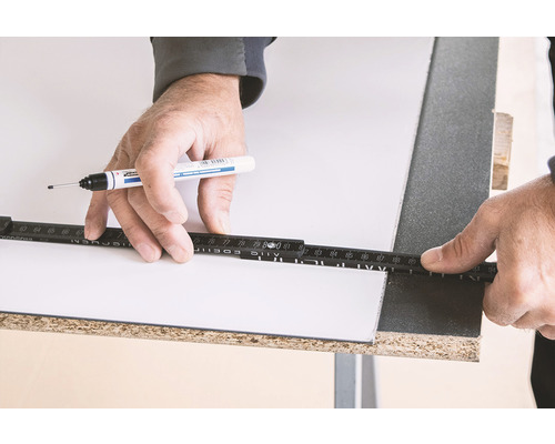 Osoba označuje dosku perom a skladacím metrom.