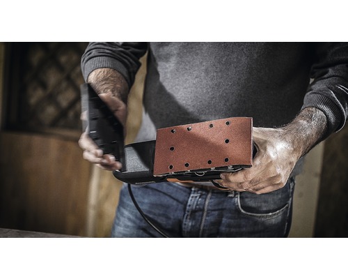 Muž drží vibračnú brúsku pripravenú na prácu.