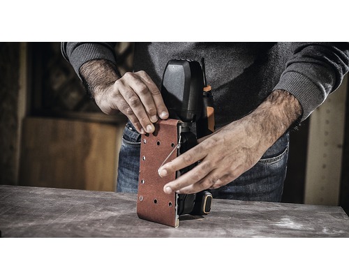 Osoba mení brúsny papier na pásovej brúske.