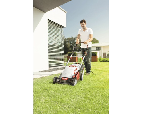 Muž kosí trávnik elektrickou kosačkou v záhrade.