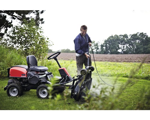 Muž čistí záhradný traktor na lúke