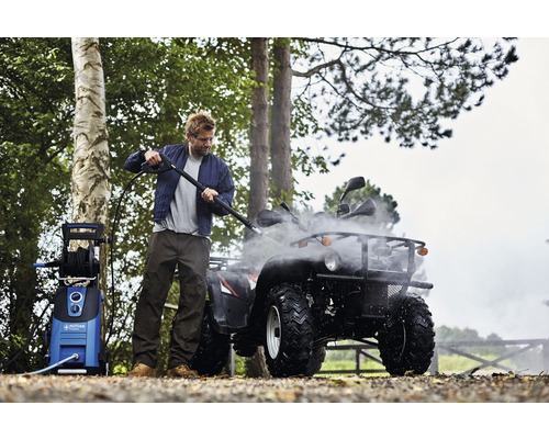 Muž čistí štvorkolku vysokotlakovým čističom vonku.