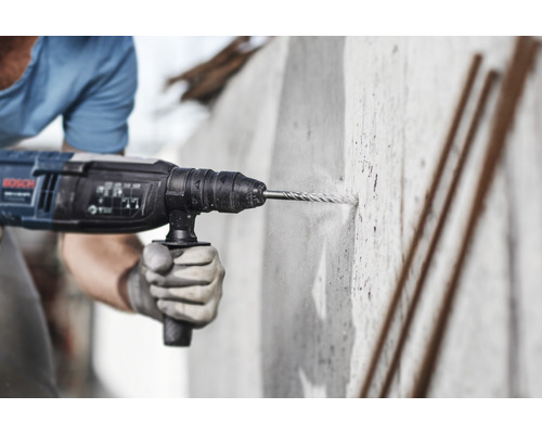 Muž vŕta dieru do betónovej steny pomocou vŕtacieho kladiva