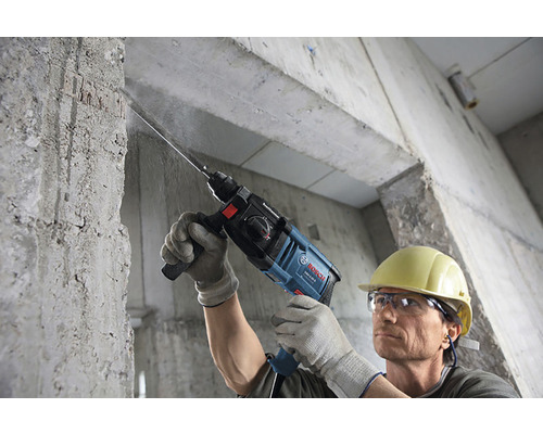 Muž vŕta s vŕtacím kladivom do betónovej steny