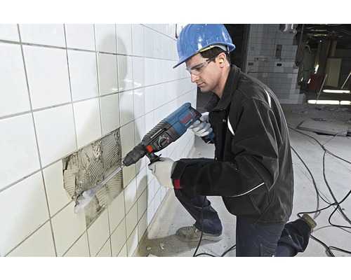 Remeselník s vŕtacím kladivom odstraňuje dlaždice zo steny.