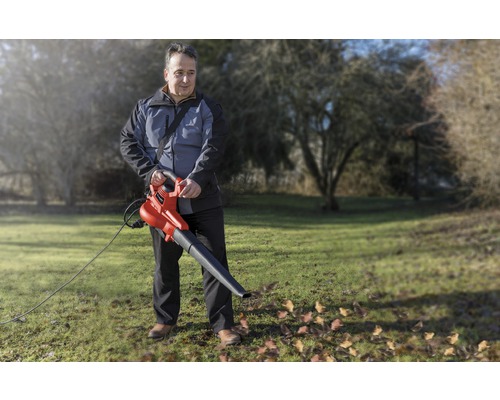 Muž používa elektrický fúkač lístia v záhrade na odstránenie lístia.