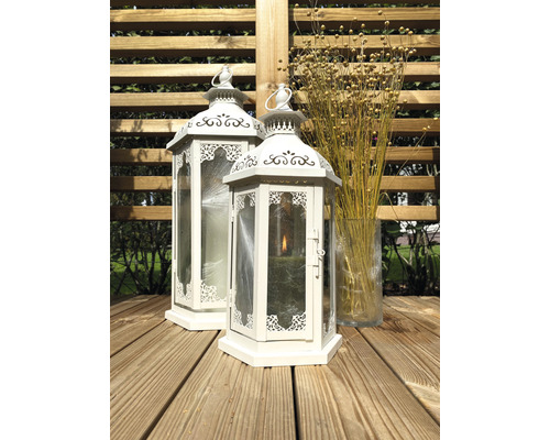 Dve biele lucerny z kovu a skla na drevenej terase, vedľa sklenená váza so sušenými kvetmi