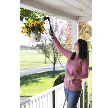 Žena zalieva visiace kvety záhradnou sprchou.