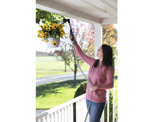 Žena zalieva visiace kvety záhradnou sprchou.