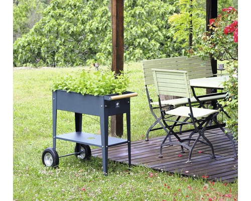 Záhradná scéna s kovovým vozíkom na bylinky, záhradným stolom a záhradnou lavicou na drevenej terase.