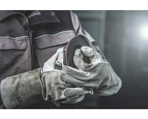 Osoba drží uhlovú brúsku s ochrannými rukavicami.