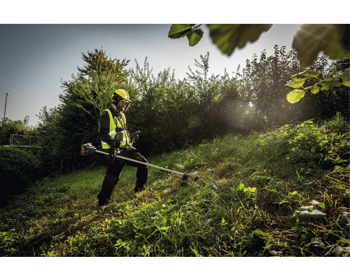 Osoba s bezpečnostným vybavením používa krovinorez na kosenie trávy