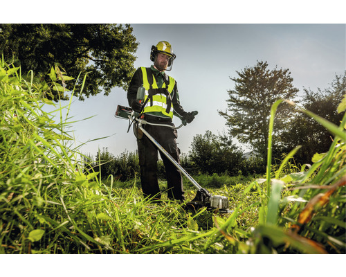 Muž kosí vysokú trávu vyžínačom a má na sebe ochranný odev.
