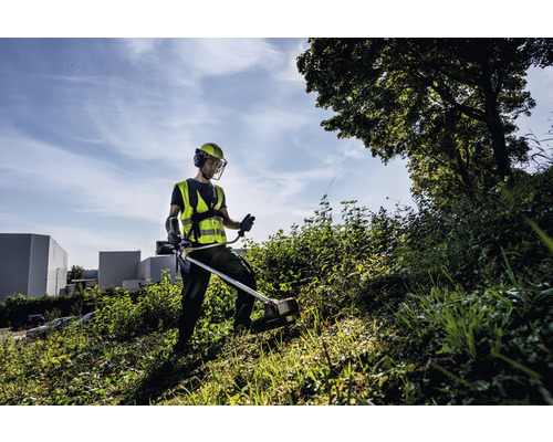 Muž pracuje s vyžínačom na lúke a má na sebe ochranný odev.