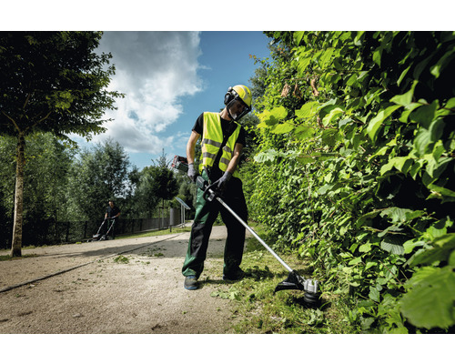 Osoba strihá živý plot v záhrade pomocou krovinorezu.