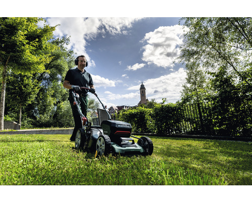 Muž kosí trávnik pomocou akumulátorovej kosačky Metabo v záhrade.