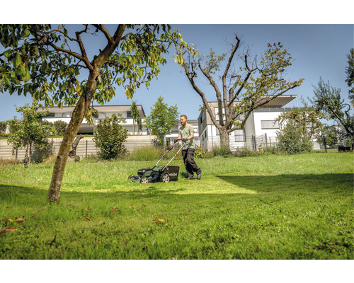 Muž kosí trávnik s kosačkou v záhrade.