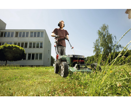 Muž so slúchadlami na ušiach kosí trávnik kosačkou Metabo