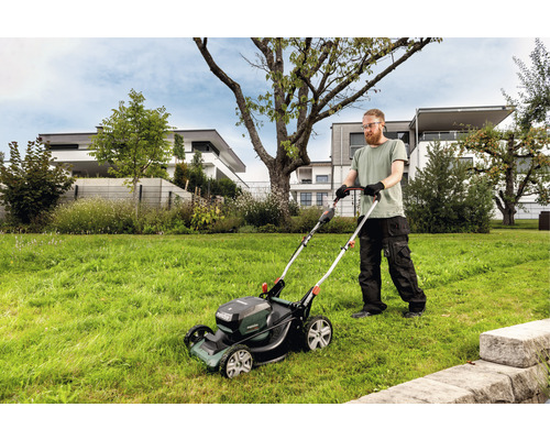 Muž kosí trávnik akumulátorovou kosačkou v záhrade.