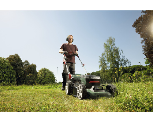 Muž kosí trávnik kosačkou na trávu Metabo v záhrade.