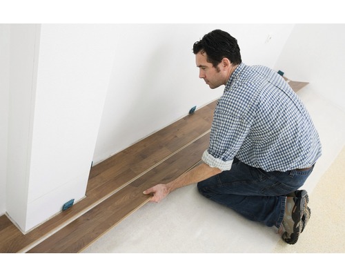 Muž kladie laminátovú podlahu v interiéri s dištančnými podložkami.