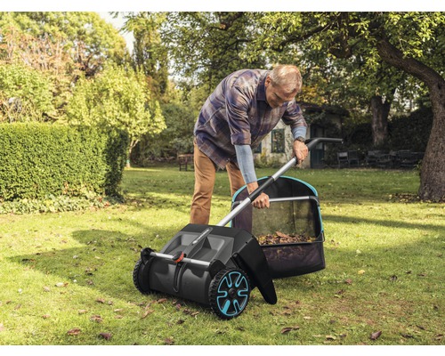 Muž používa zametací stroj na trávnik v záhrade na zber lístia.