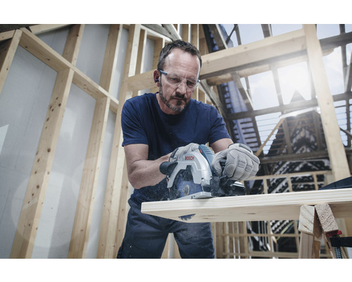 Muž reže drevenú dosku ponornou pílou Bosch v svetlej dielni.