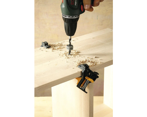 Vŕtačka vŕta do drevenej dosky upevnenej pomocou uhlovej svorky.