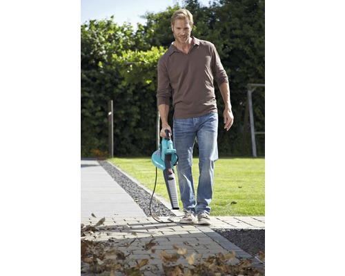 Muž čistí záhradný chodník pomocou fúkača lístia.