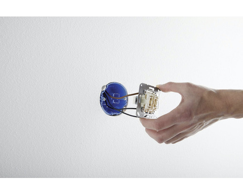 Ruka montuje vypínač svetla do nástennej krabice.