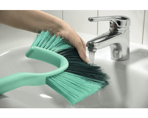 Ruka pod kohútikom s čistiacou kefou v umývadle