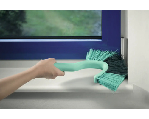 Ruka čistí rám okna pomocou kefy na okenné rámy.