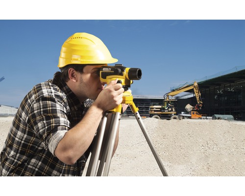Stavebný robotník s ochrannou prilbou používa nivelačný prístroj na stavenisku.