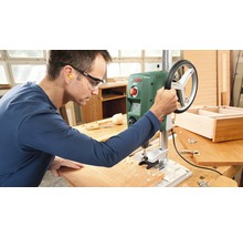 Muž obsluhuje stolnú vŕtačku v dielni.