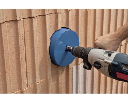 Vŕtací stroj vŕta otvor do tehlovej steny pomocou dierovky.