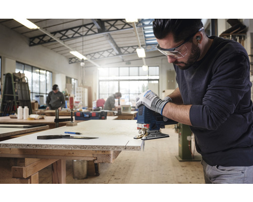 Muž reže obrobok priamočiarou pílou v dielni.