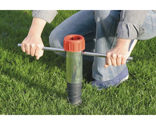 Osoba používa nástroj na zatĺkanie do pôdy v tráve