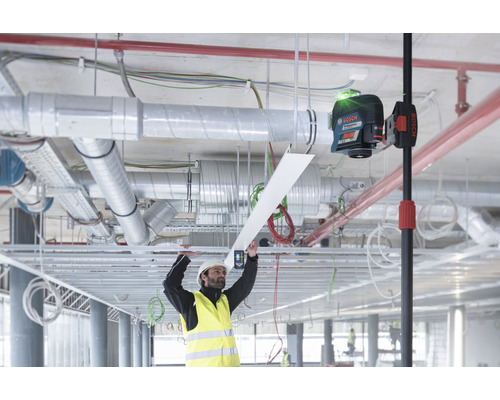 Pracovník s ochrannou prilbou a výstražnou vestou montuje strop pomocou laserovej vodováhy Bosch.