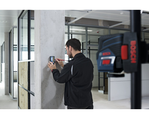 "Muž používa digitálny merač na betónovej stene