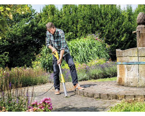Muž odstraňuje burinu elektrickým odstraňovačom škár na dláždenom povrchu v záhrade.