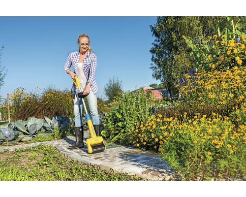 Žena odstraňuje burinu elektrickou kefou na škáry na záhradnom chodníku.