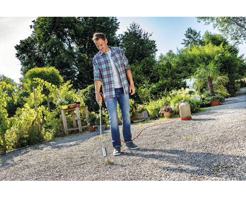 Muž používa plynový horák na ničenie buriny v záhrade.