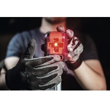 Osoba drží v ruke stavebný laser s červenými laserovými lúčmi.